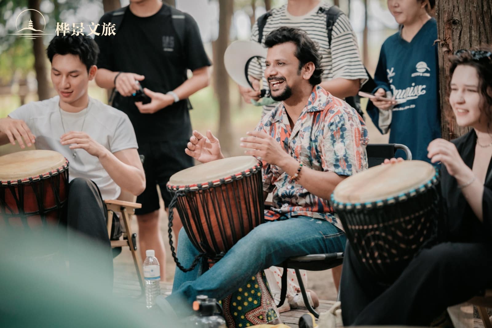 Participants playing hand drums in the shade at Qingshan Lake