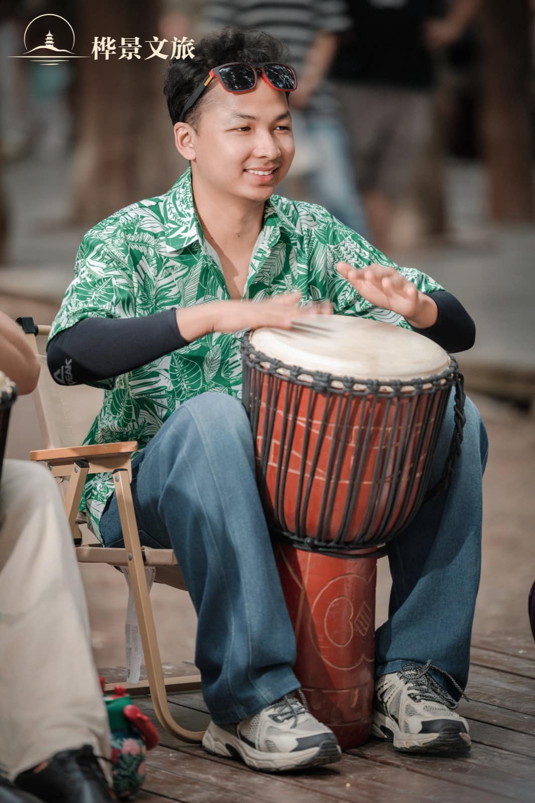 A participant in a green floral shirt playing a hand drum
